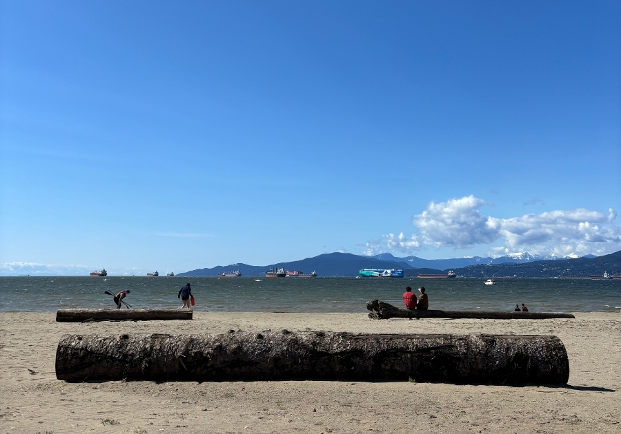 バンクーバーのキツラノビーチから見える穏やかな海と山の風景。晴れた空の下、人々が浜辺でリラックスしている様子。