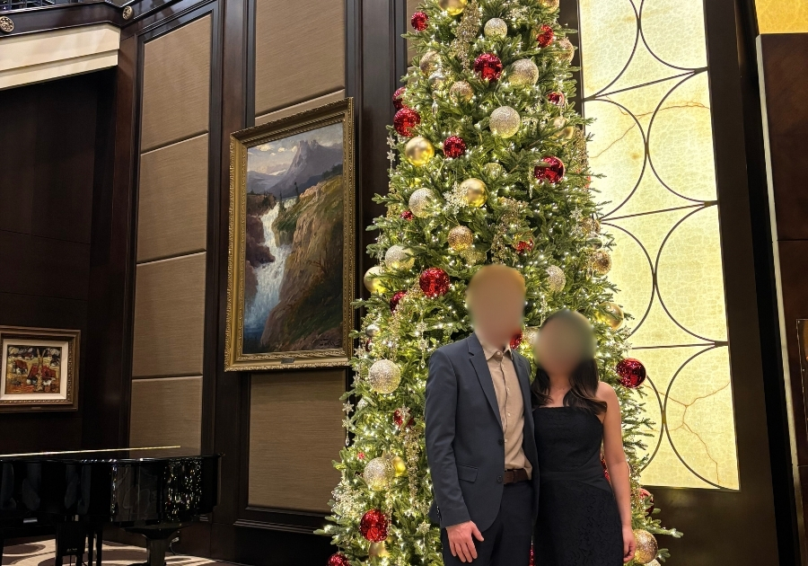 クリスマスツリーの前に立つカップルの画像。