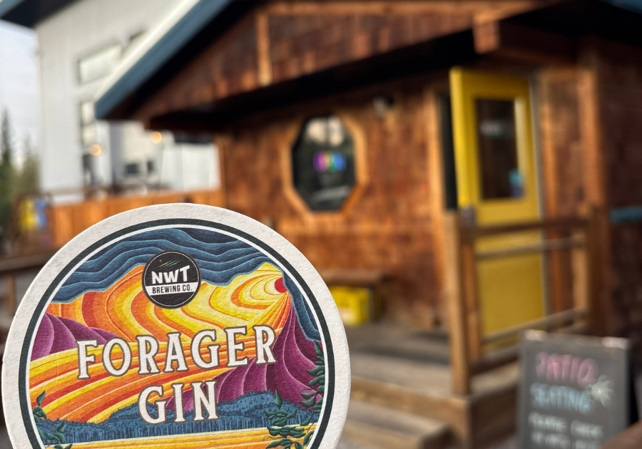 NWT Brewing Company のカラフルなコースターを手に持ち、木造の店舗外観が背景に写る様子