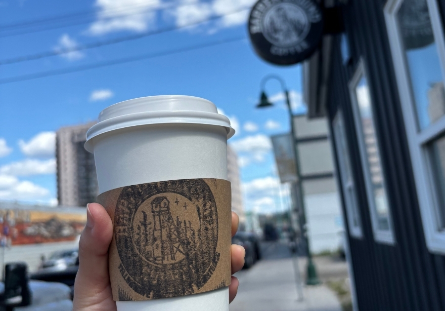 Barren Ground Coffee の紙カップを手に持ち、青空の下で店舗の看板が見える様子
