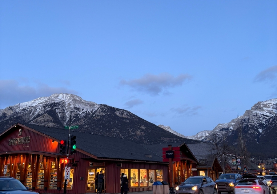 冬のキャンモアのメインストリート。雪山を背景に、赤い外観のショップと街灯が並ぶ夕方の風景。